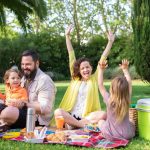 Happy family enjoying a sunny picnic with children on a blanket in a Portugal park.